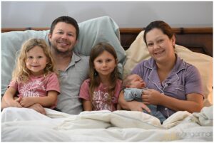 Family cuddling in bed as doula takes photos