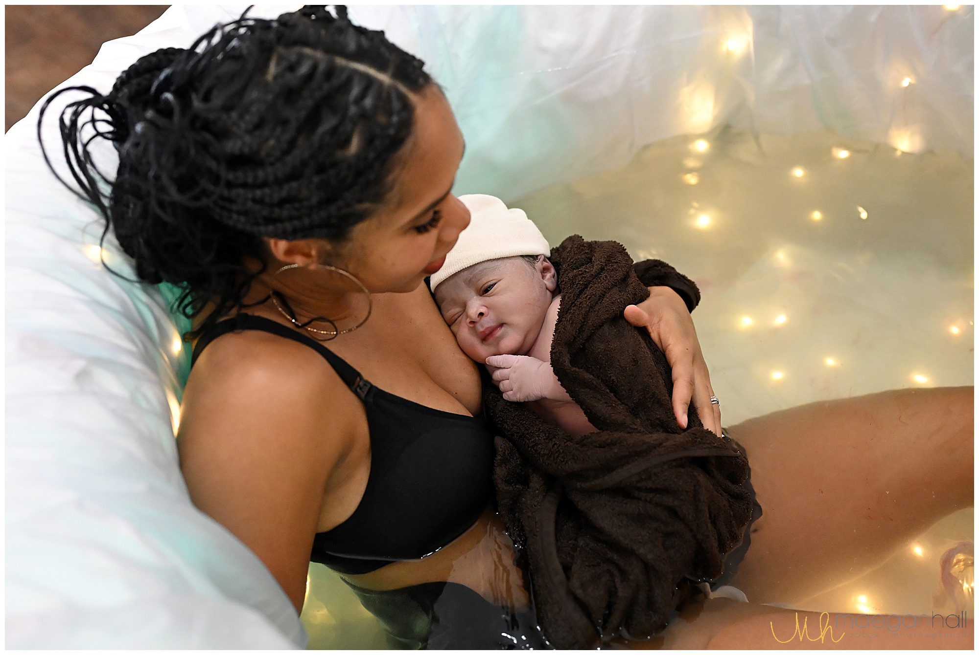 mom sits in birth tub while baby looks up at her